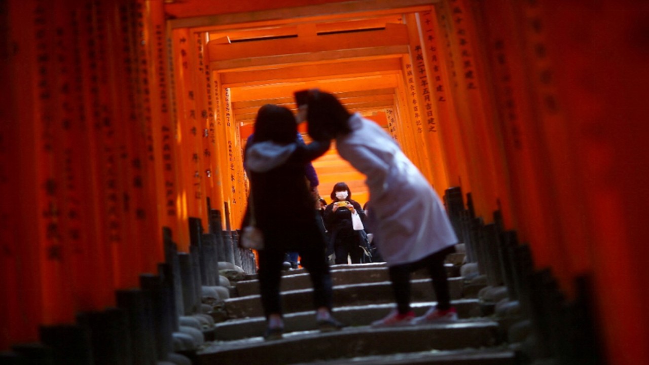 Pengunjung mengenakan masker pasca merebaknya penyakit coronavirus (COVID-19), menjelajahi gerbang kayu torii di kuil shinto Fushimi Inari Taisha di Kyoto, Jepang 13 Maret 2020. (foto: REUTERS/Edgard Garrido)