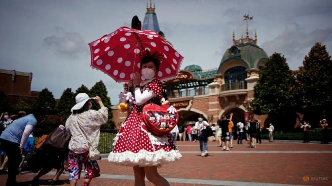 Seorang pengunjung yang mengenakan masker berpose di Shanghai Disney Resort, saat taman hiburan Shanghai Disneyland dibuka kembali setelah ditutup karena wabah Covid-19 di Shanghai, China pada 30 Juni 2022. (Aly Song/Reuters)