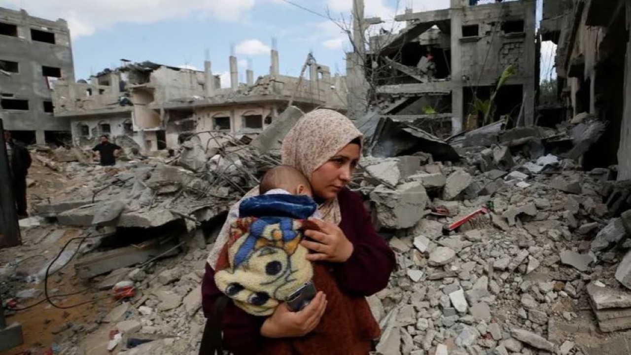 Seorang wanita Palestina menggendong anaknya di tengah puing-puing rumah mereka yang dihancurkan oleh serangan udara Israel selama pertempuran Israel-Hamas di Gaza 23 Mei 2021. (Reuters)