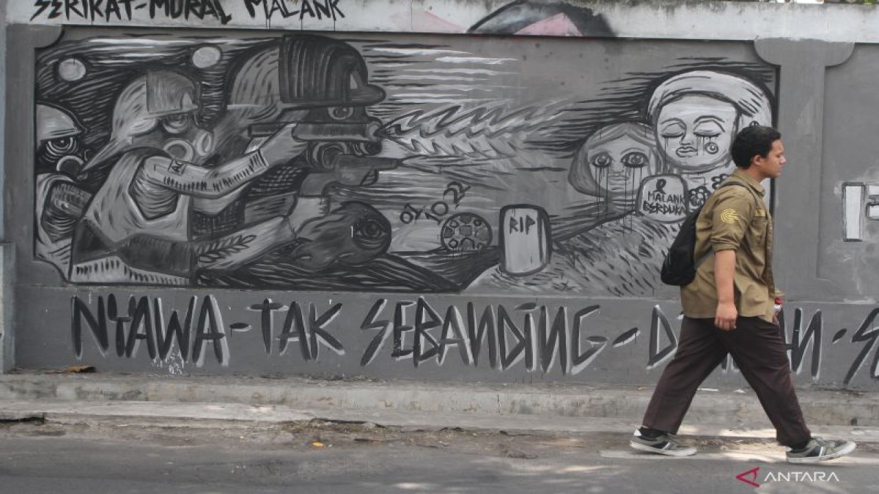 Pejalan kaki melintasi mural bertema tragedi Kanjuruhan di Jalan Sigura-gura, Malang, Jawa Timur, Jumat (14/10/2022). (ANTARA FOTO/ARI BOWO SUCIPTO)