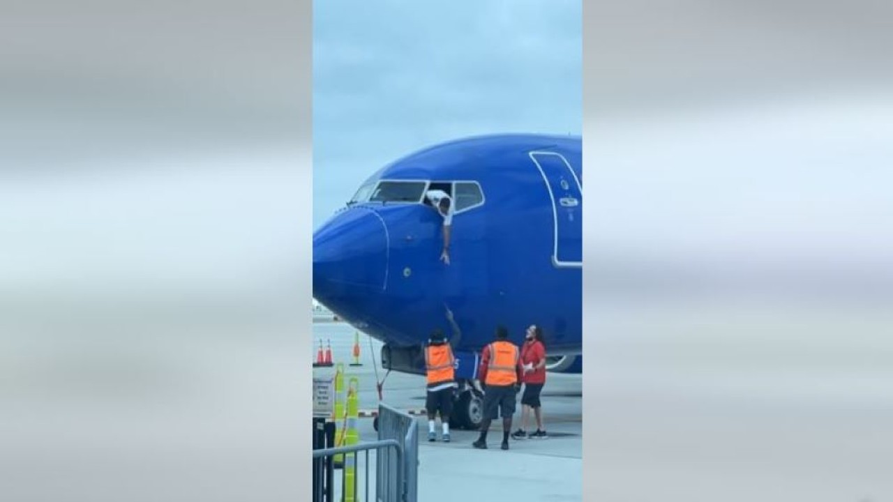 Pilot kapten penerbang tertangkap kamera mengambil ponsel penumpang yang tertinggal dari jendela kokpit pesawat. (Tangkapan layar)