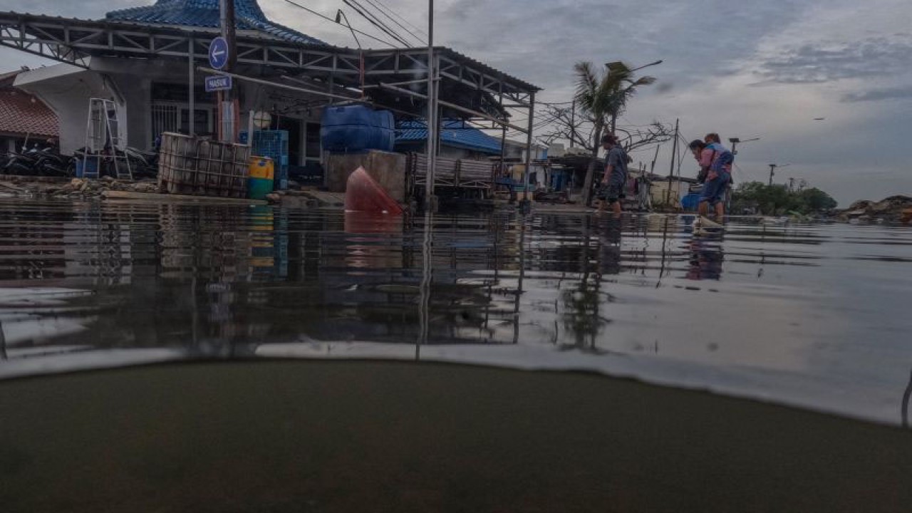 Warga melintasi jalan yang terendam limpasan air laut ke daratan atau rob di Pelabuhan Muara Baru Jakarta, Rabu (28/12/2022).ANTARA FOTO/Wahyu Putro A/foc.