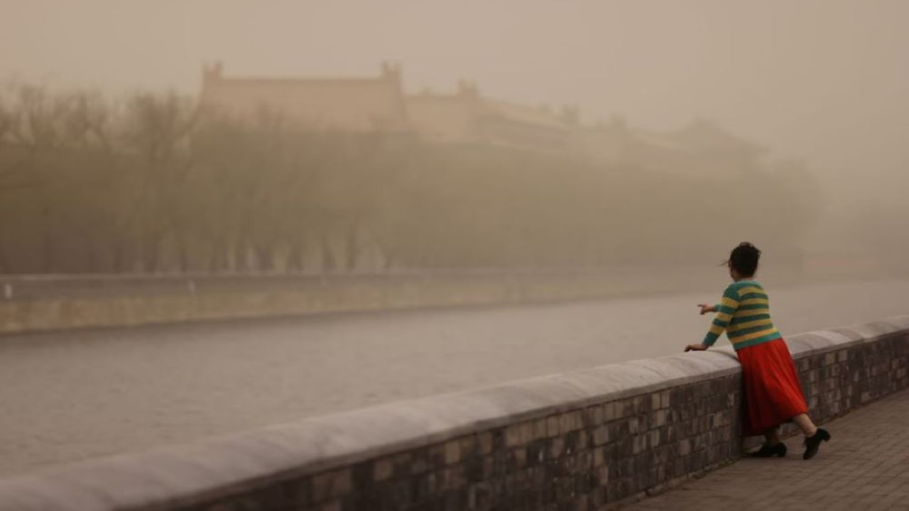 Seorang wanita berpose di dekat Forbidden City, saat kota itu diselimuti kabut asap di tengah badai pasir, di Beijing, China, 10 Maret 2023. (Tingshu Wang/Reuters)