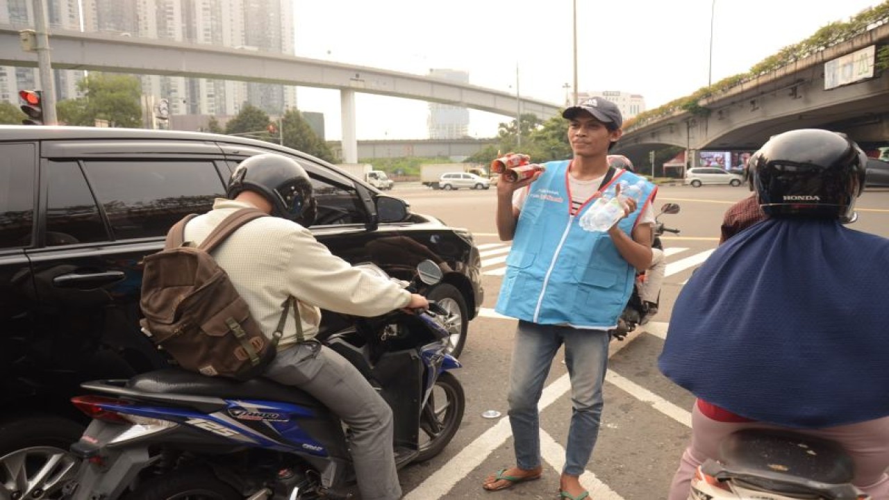 Seorang pedagang asongan mengenakan rompi yang terbuat dari daur ulang sampah plastik kemasan PET tengah menjajakan minuman kepada para pengendara di Tomang, Jakarta Barat, Senin (5/6/2023). ANTARA/HO-Le Minerale