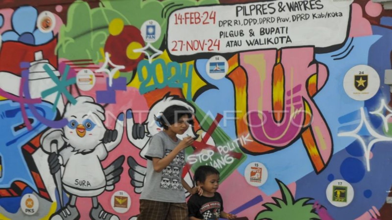 Dua anak berjalan melintasi mural Pemilu 2024 di Pandeglang, Banten, Senin (6/3/2023). Mural tersebut bertujuan untuk mengajak warga berpartisipasi dalam menyukseskan Pemilu 2024 serta menolak politik uang. (ANTARA FOTO/Muhammad Bagus Khoirunas/rwa.)
