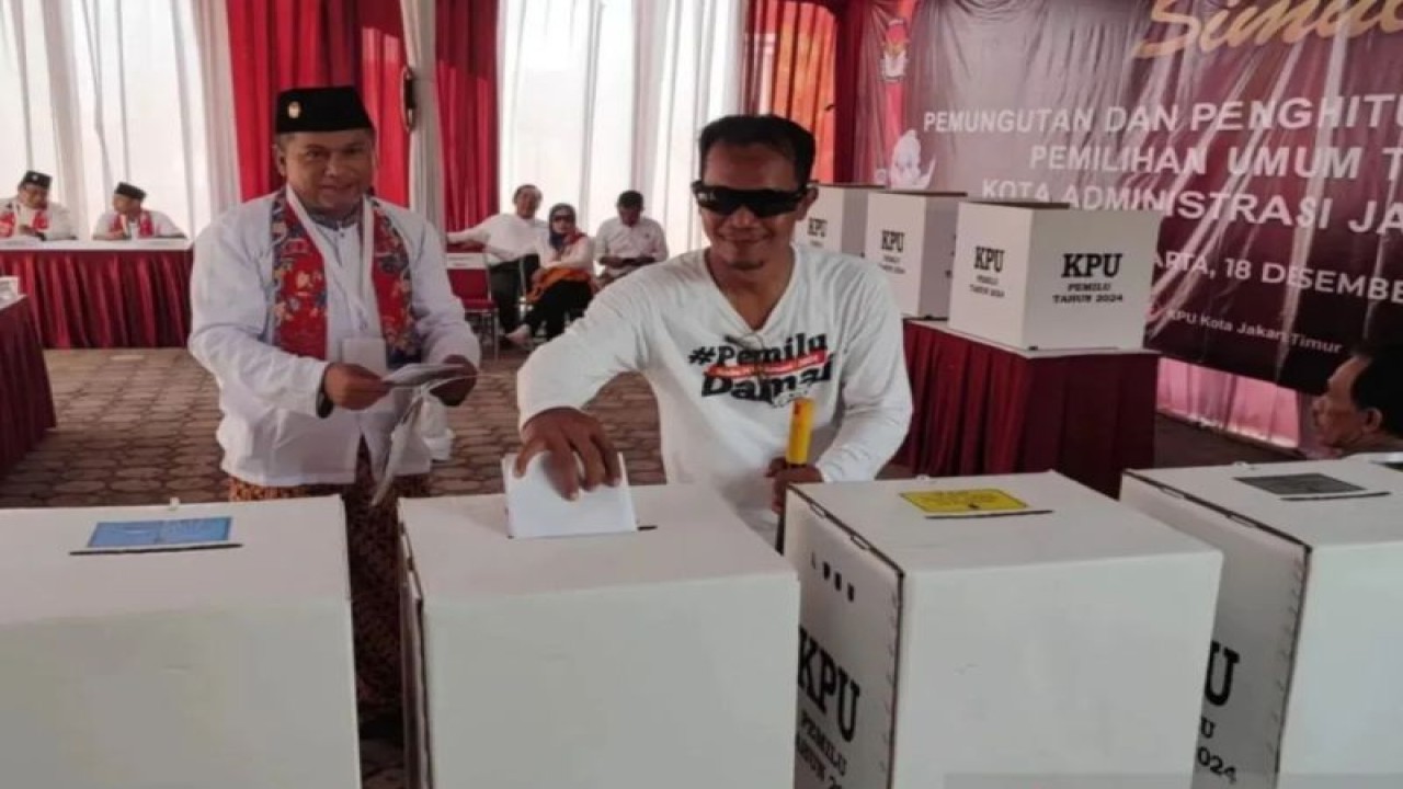 Petugas Kelompok Penyelenggara Pemungutan Suara (KPPS) mendampingi salah satu warga tuna netra saat memasukan surat suara ke kotak suara dalam simulasi pemungutan dan penghitungan suara Pemilu 2024 di Kantor KPU Jakarta Timur, Pulogadung, Senin (18/12/2023). (ANTARA/Syaiful Hakim)