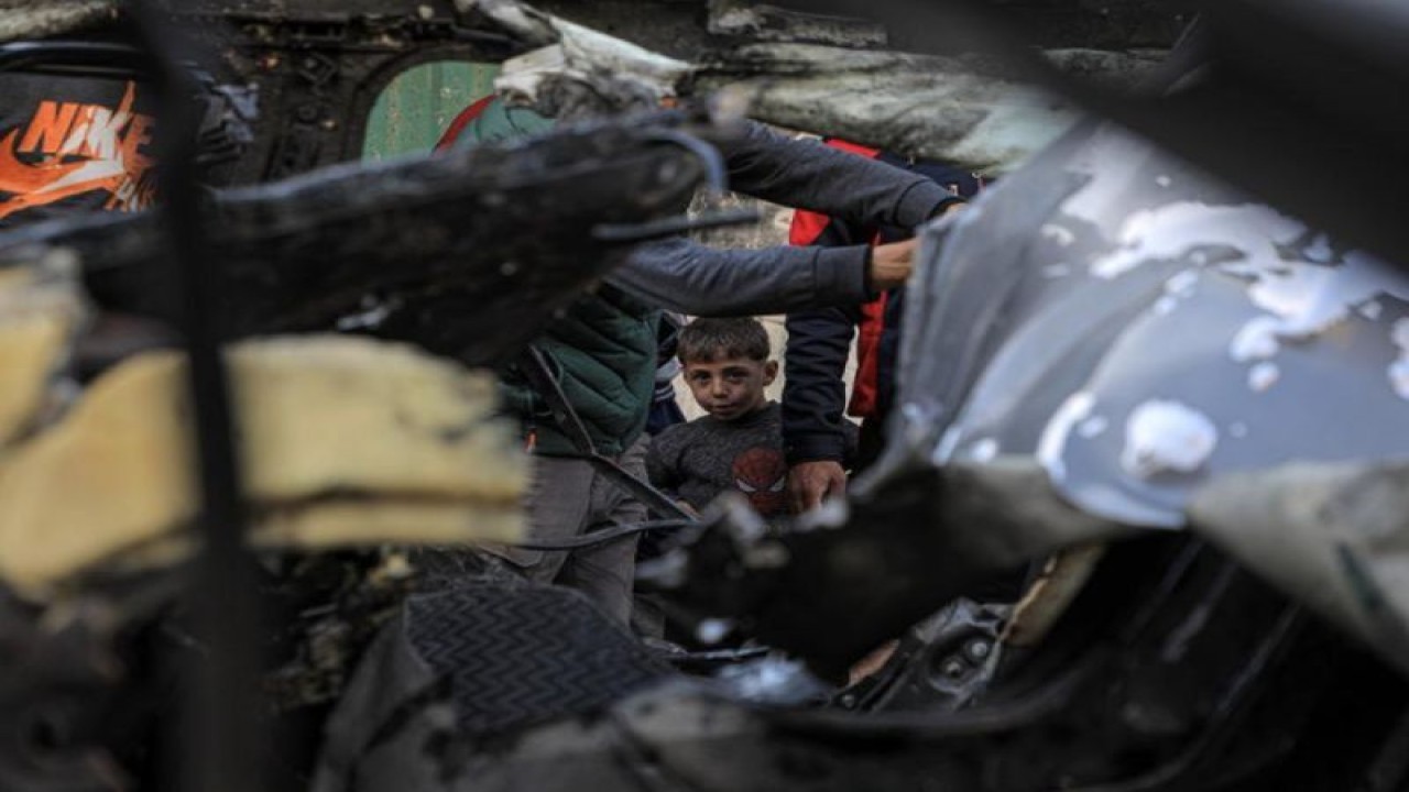 Seorang anak laki-laki memandangi kendaraan yang hancur akibat serangan udara Israel di kota Rafah di Jalur Gaza selatan, pada 8 Januari 2024. (Xinhua/Rizek Abdeljawad) (Xinhua/Rizek Abdeljawad)