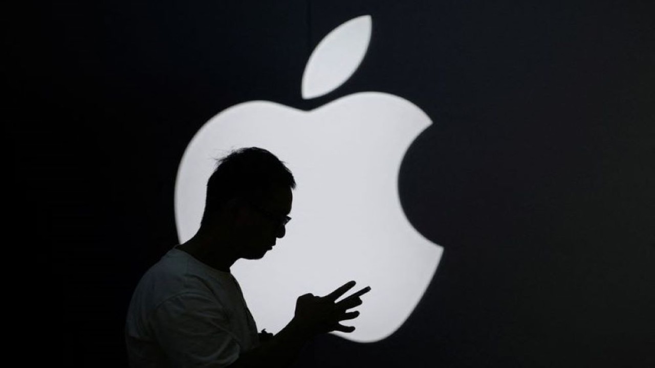 Seorang pria memeriksa ponselnya di dekat logo Apple di Shanghai, China, pada 13 September 2023. (Foto: Aly Song/Reuters)