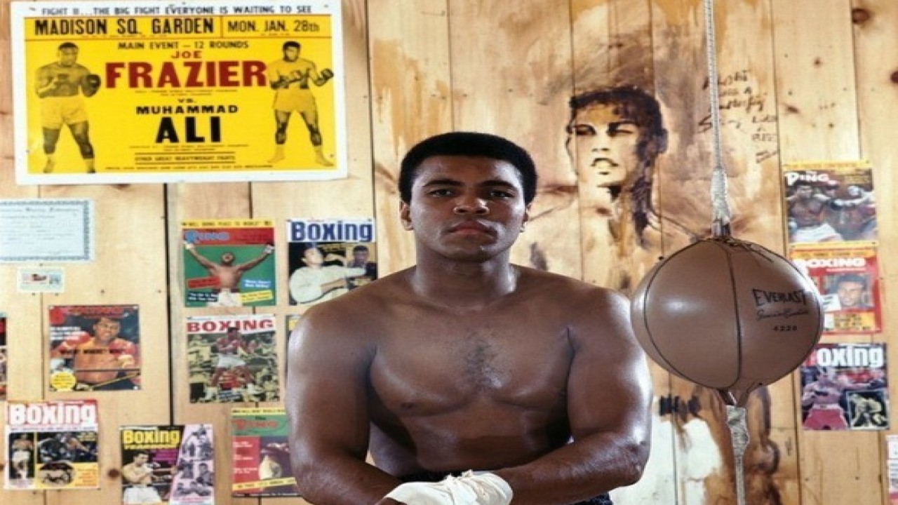 Muhammad Ali berpose di depan pamflet pertarungannya melawan Joe Frazier. (Instagram)