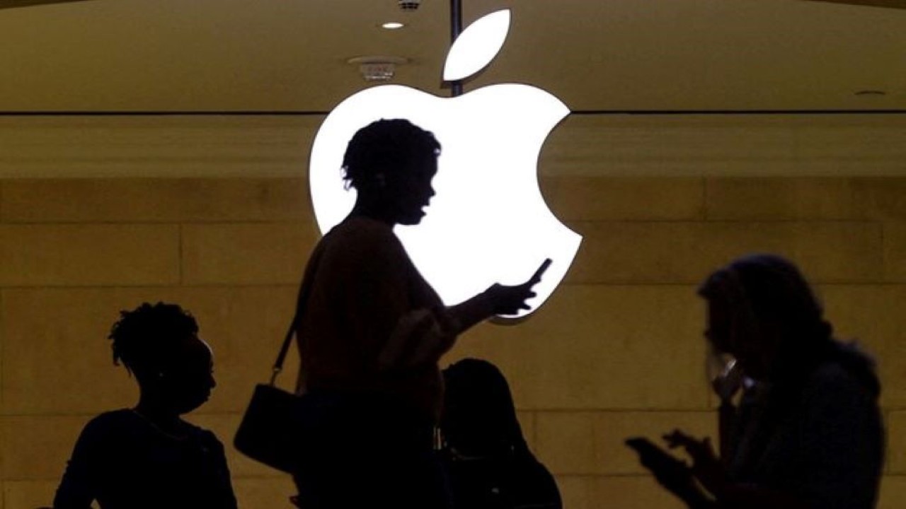 Seorang wanita menggunakan perangkat seluler iPhone saat dia melewati logo Apple yang menyala di toko Apple di Grand Central Terminal di New York City, Amerika Serikat, 14 April 2023. (Foto: Dok/Mike Segar/Reuters)