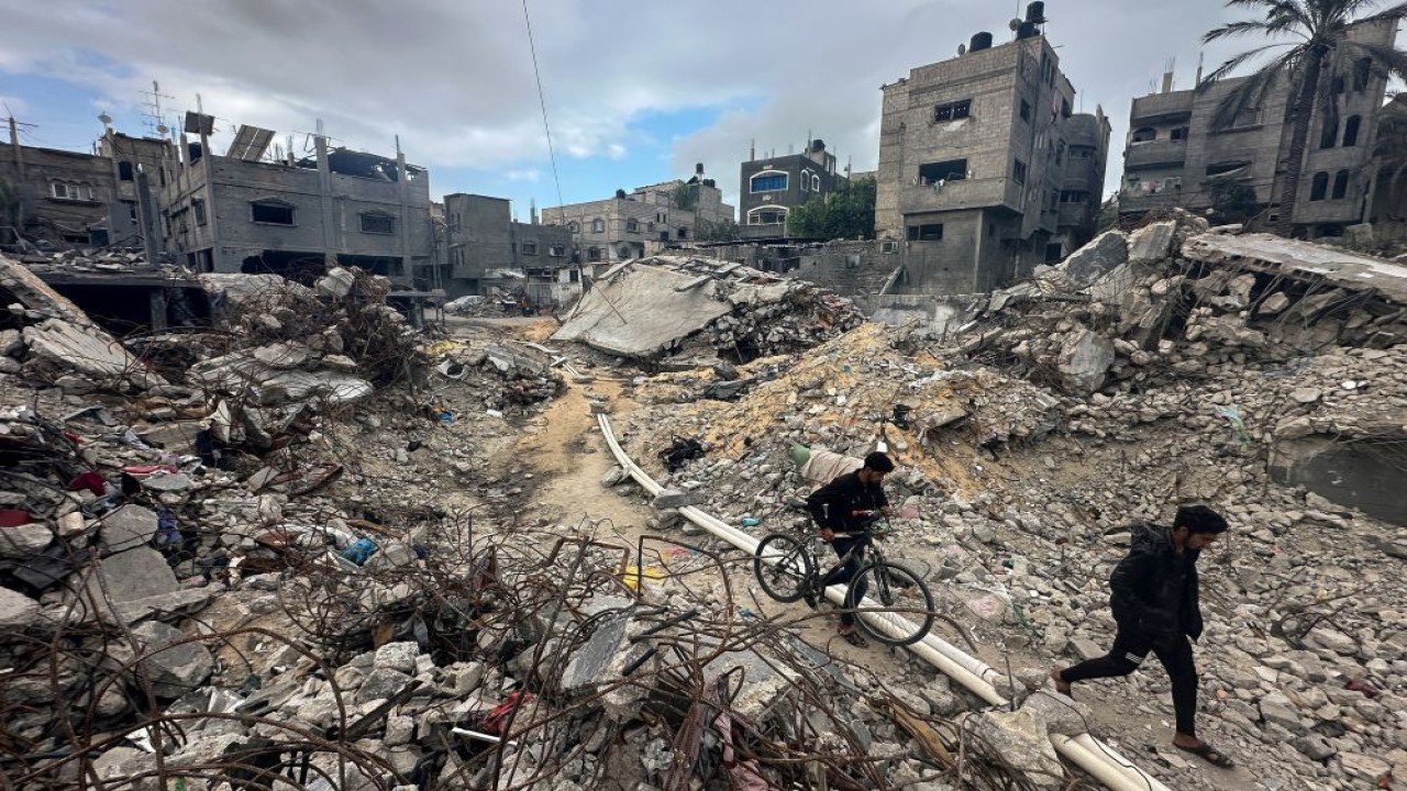 Warga Palestina melintas di antara bangunan tempat tinggal yang hancur akibat serangan Israel. (Foto: Reuters)